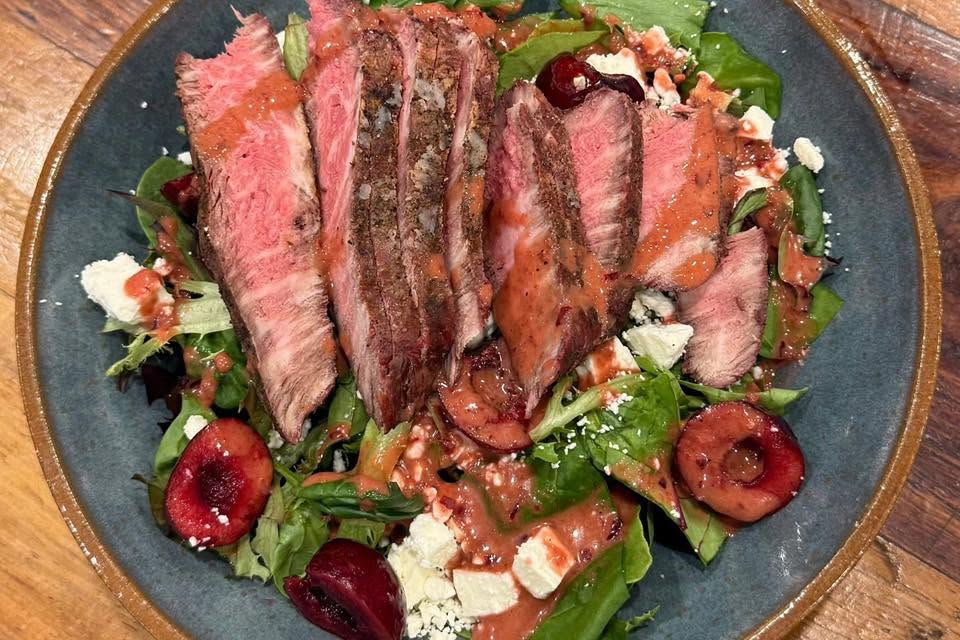 Sliced Wagyu steak over a fresh greens, cherry and feta salad